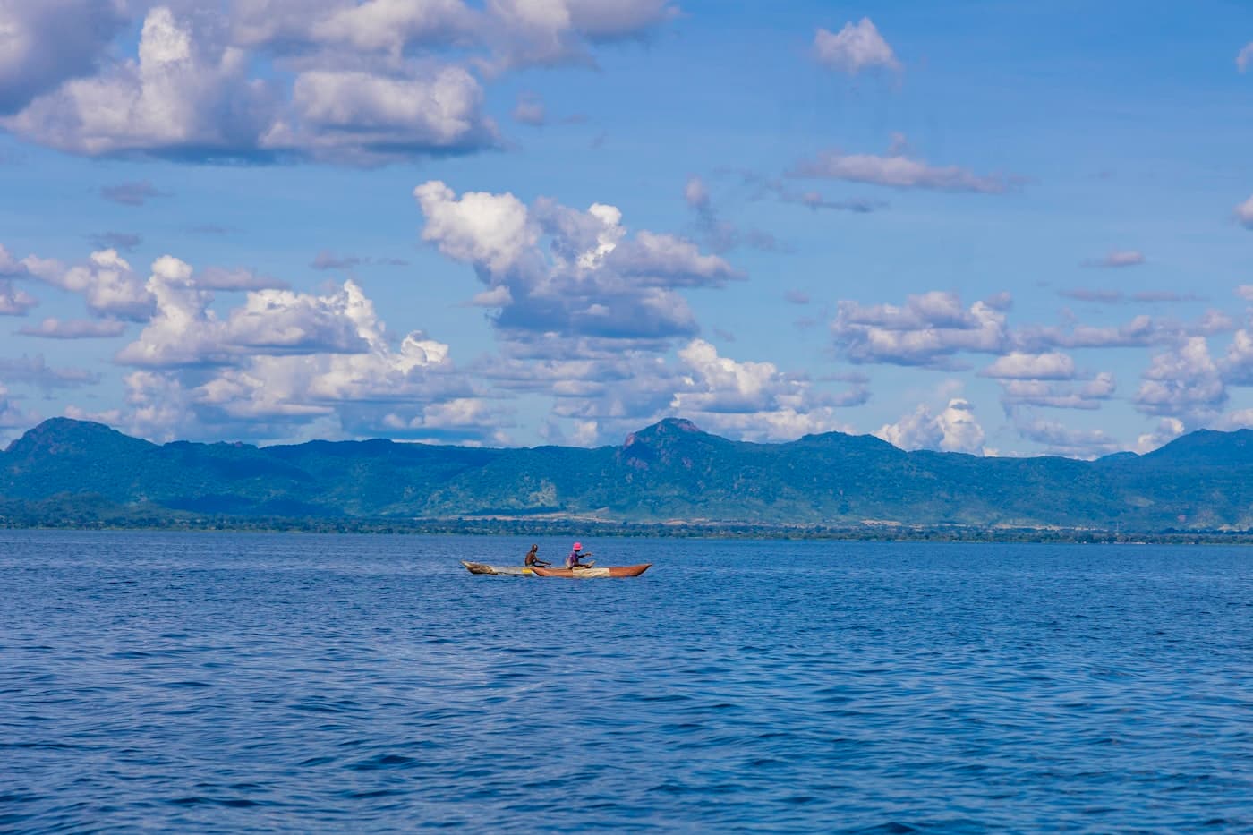 Two people kayak on a calm blue lake near mountains