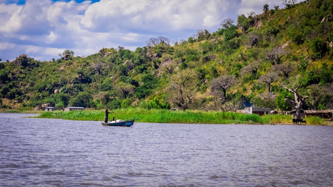 A small boat floating on top of a river next to a lush green hillside